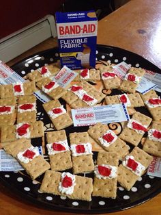 a black plate topped with crackers covered in red and white frosting next to a box of band aid