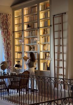 a woman standing in front of a book shelf filled with books and looking out the window