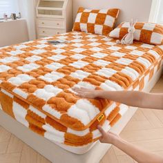 a person is holding up an orange and white checkered bedspread on a bed