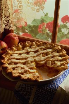 a pie sitting on top of a white plate next to an apple and flowered window sill