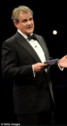 a man in a tuxedo holds out his hand as he stands on stage