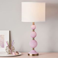 a pink lamp sitting on top of a table next to a white plate and pen holder