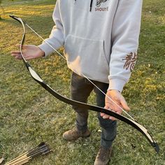 a young man holding onto a bow and arrow in the grass with another person standing next to him