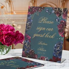 there is a vase with flowers next to a sign on the table that says please sign out guest book