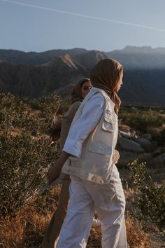 two women walking in the desert with mountains in the background