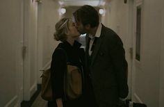 a man and woman kissing while standing in an open doored hallway with luggage on the floor