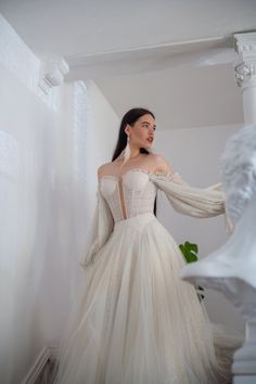 a woman in a white wedding dress standing next to a bustle wearing an off the shoulder long sleeved gown