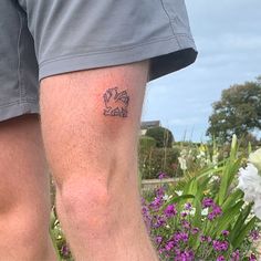 a man with a tattoo on his leg standing next to flowers and purple wildflowers