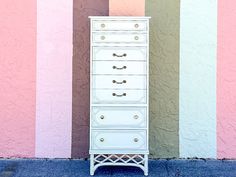 a tall white dresser sitting in front of a colorful wall