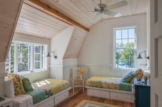 two beds in a room with wooden floors and white walls, one has a ceiling fan