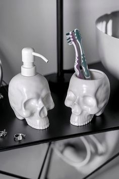 two skull shaped soap dispensers with toothbrushes in them on a table