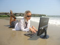 a woman laying on the beach using a laptop computer