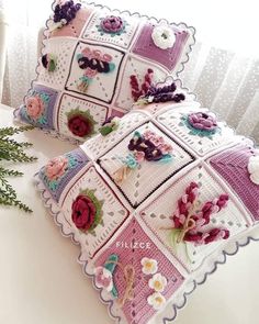 two crocheted pillows sitting on top of a white table next to a plant