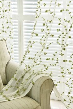 a white chair sitting in front of a window covered with a green flowered curtain