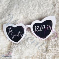 a pair of heart shaped sunglasses with the date and time printed on them, sitting on a fluffy white surface