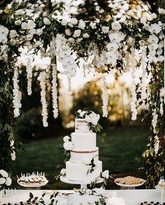 a white wedding cake sitting on top of a table next to a lush green field