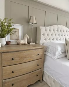 a white bed sitting next to a wooden dresser with pillows on top of it in a bedroom