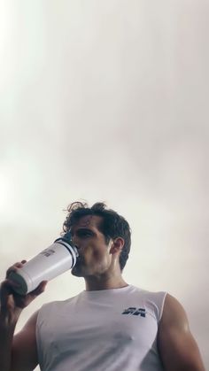 a man drinking from a water bottle while standing in front of a white sky with clouds