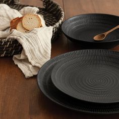 two black plates sitting on top of a wooden table next to a basket filled with bread