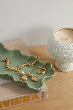 a green tray with gold chains on it next to a candle holder and a book