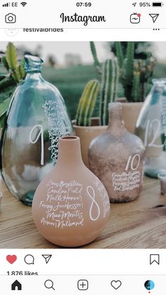 several vases with writing on them sitting on a table next to cacti