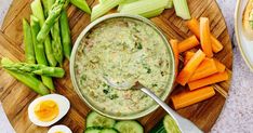 a bowl of dip surrounded by vegetables on a wooden platter with hard boiled eggs and asparagus