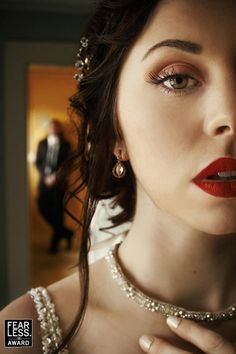 a woman with red lipstick and pearls on her neck is posing for a photo in front of a man