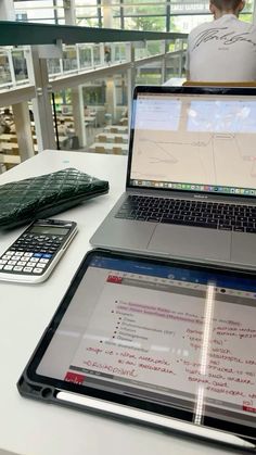 an open laptop computer sitting on top of a white table next to a calculator