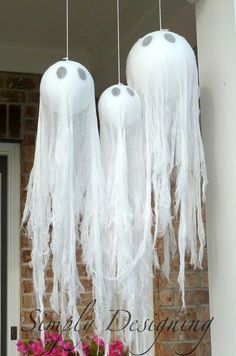 three white chandeliers hanging from a brick building with flowers in the foreground