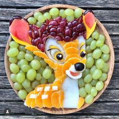 a plate with grapes, oranges and grapes in the shape of a deer on it