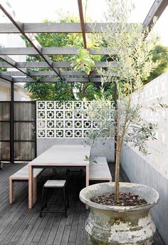 an outdoor table and bench with a tree in the center on a wooden deck surrounded by greenery