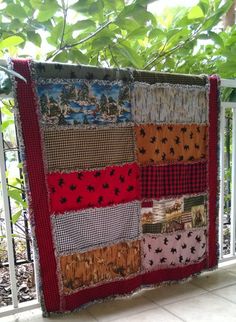 a quilt hanging on the side of a fence with trees in the backgroud