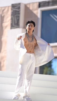 a man with no shirt and white pants is posing for a photo in front of a building