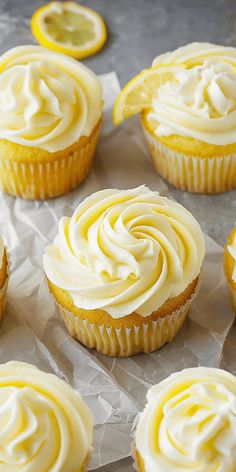 cupcakes with white frosting and lemon slices on the side, sitting on wax paper