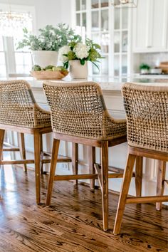 three wicker bar stools sit at the center of a kitchen island with potted plants on it