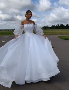 a woman in a white wedding dress is standing on the road with her arms behind her back