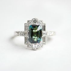 Item Details: 3.58 carat color change blue-green emerald cut sapphire Fourteen round brilliant cut diamonds 0.25 ct (G/VS) Two carre cut diamonds 0.14 ct (G/VS) Six baguette cut diamonds 0.36 ct (G/VS) Crafted in Platinum This ring was custom created with a one-of-a-kind center stone. Email custom@berlingerrings.com to create a similar ring. Enquire about this ring Design a custom piece with us Change Blue, Sapphire Halo Engagement Ring, Sapphire Engagement Ring Halo, Wedding Rings Emerald Cut, Emerald Ring Vintage, Topaz Engagement Ring, Baguette Cut Diamond, Jewelry Images, Baguette Cut