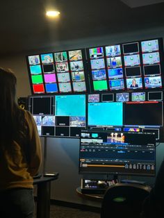 a woman is looking at multiple television screens