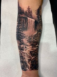 a man's arm with a waterfall and trees on it