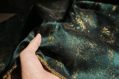 a hand is holding onto a green fabric with gold speckles on it,