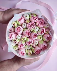 a person holding a bowl filled with pink flowers on top of a pink table cloth