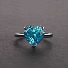 a heart - shaped blue diamond ring on a black surface, with the center stone set in silver