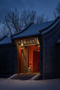 an entrance to a building at night with snow on the ground and trees in the background