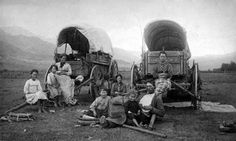 an old black and white photo of people sitting on the ground next to two wagons