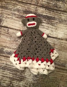 a crocheted sock monkey is sitting on a wooden surface wearing a red and white dress