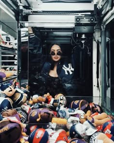 a woman standing in front of a pile of stuffed animals and baseball caps on display