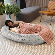 a woman laying on top of a dog bed with a cat sleeping in the middle