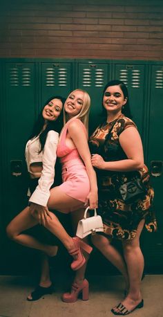 three young women posing for the camera in front of lockers with one holding a purse