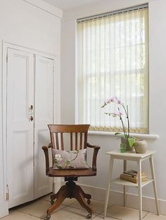 a chair sitting in front of a window next to a table with flowers on it