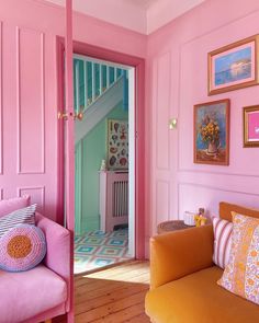 a living room with pink walls and yellow couches in the corner, along with pictures on the wall